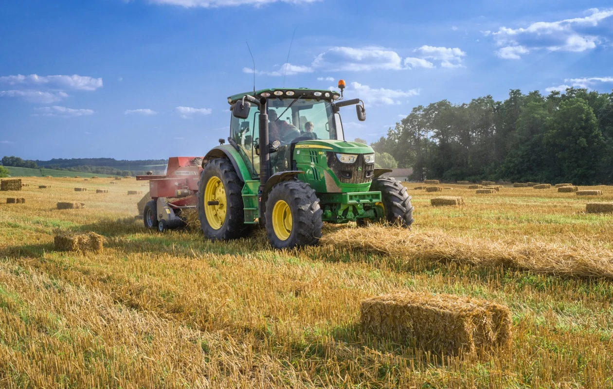 Grüner Traktor mit Ballenpresse auf einem Stoppelfeld